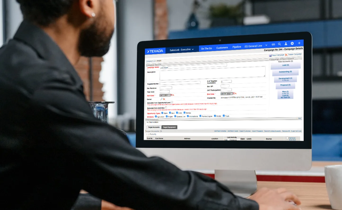 Man in a dark shirt seated at a desk, using a desktop computer displaying a data-entry form in business software.