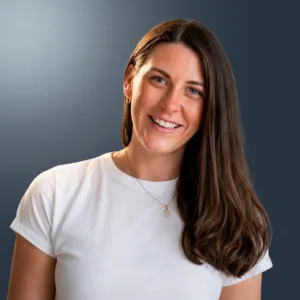 Portrait of a smiling woman with long brown hair, wearing a white t-shirt against a dark blue gradient.